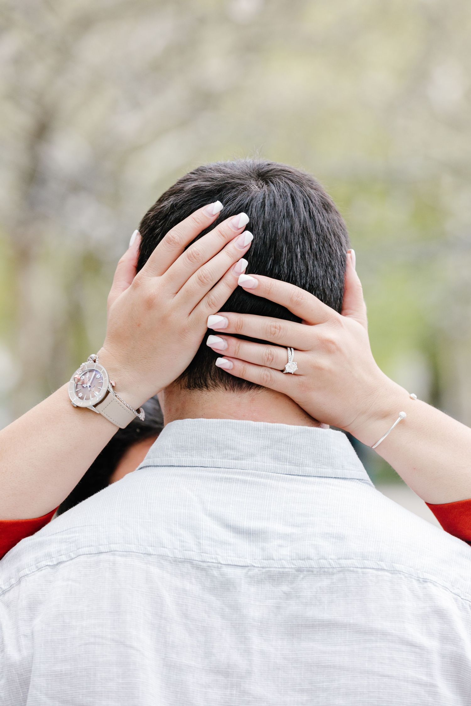 Close-up of a woman\u2019s hands with an engagement ring resting on her partner\u2019s head from behind.