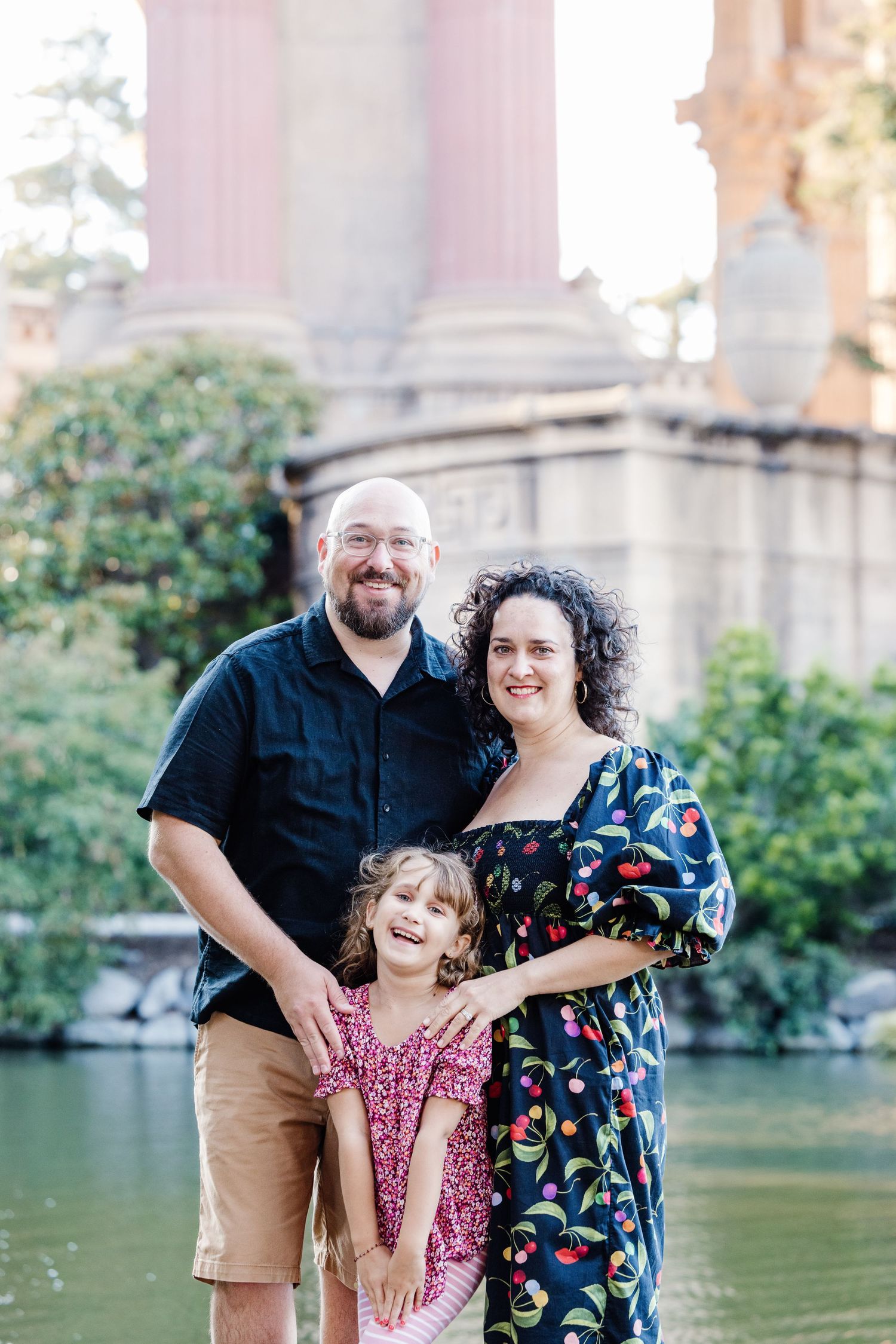 Smiling family of three poses together at the Palace of Fine Arts in San Francisco.