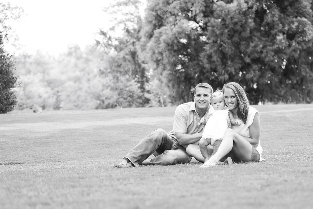 Black and white photo of a happy couple sitting together on a lush green lawn with trees in the background.