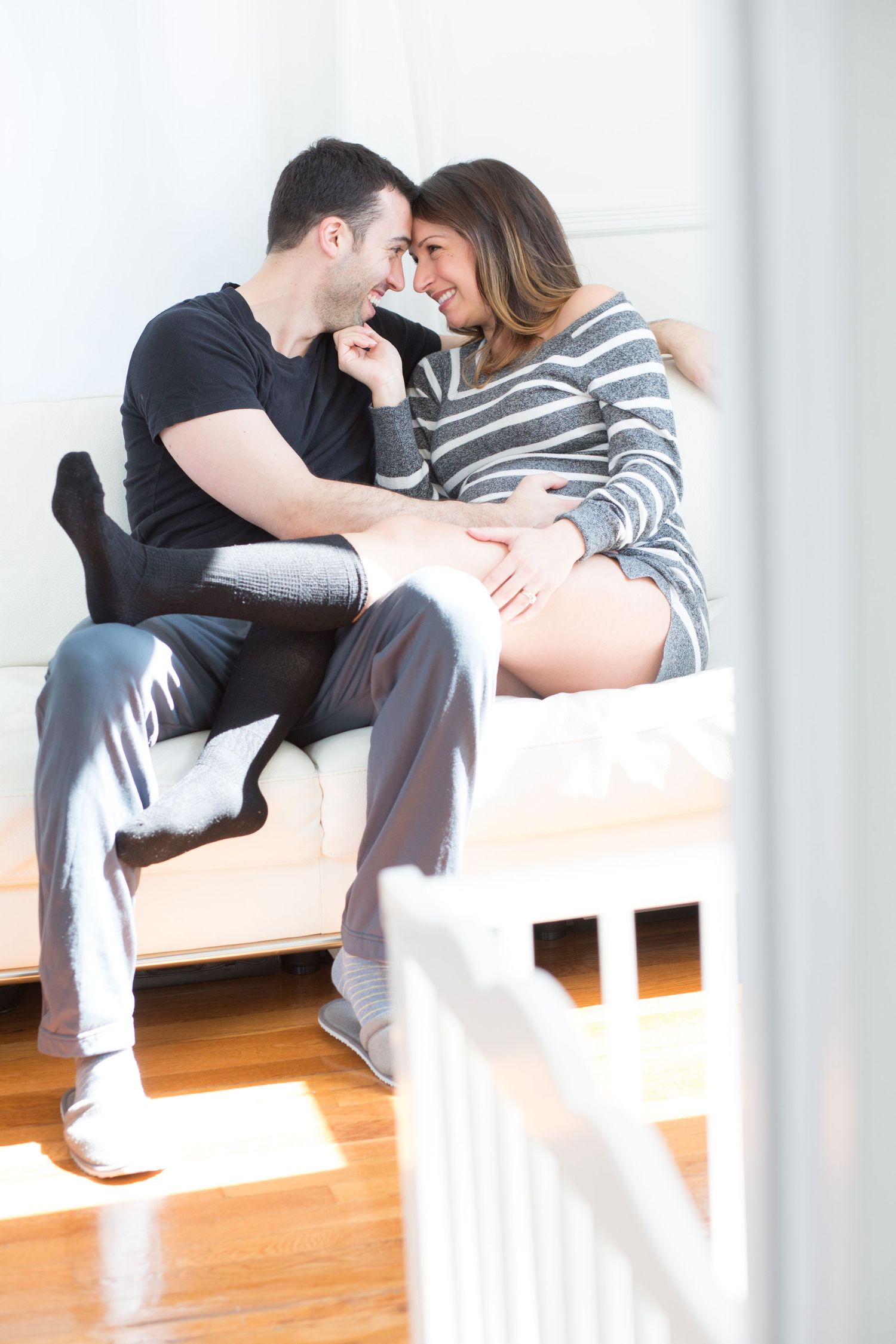 Couple sharing a tender moment on a bed, with the woman visibly pregnant, smiling and touching foreheads.