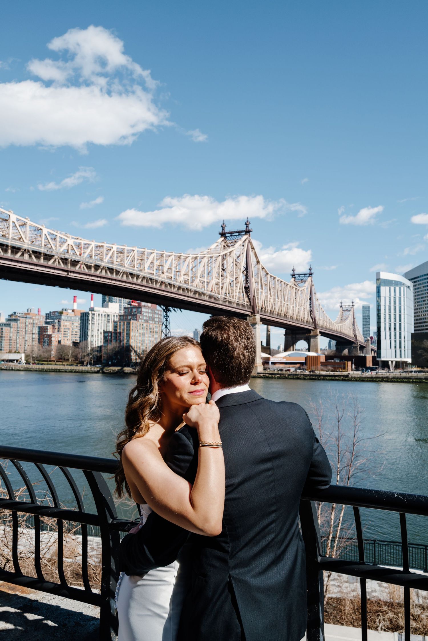 Bride and groom embracing near a railing with the Queensboro Bridge and NYC skyline behind them.