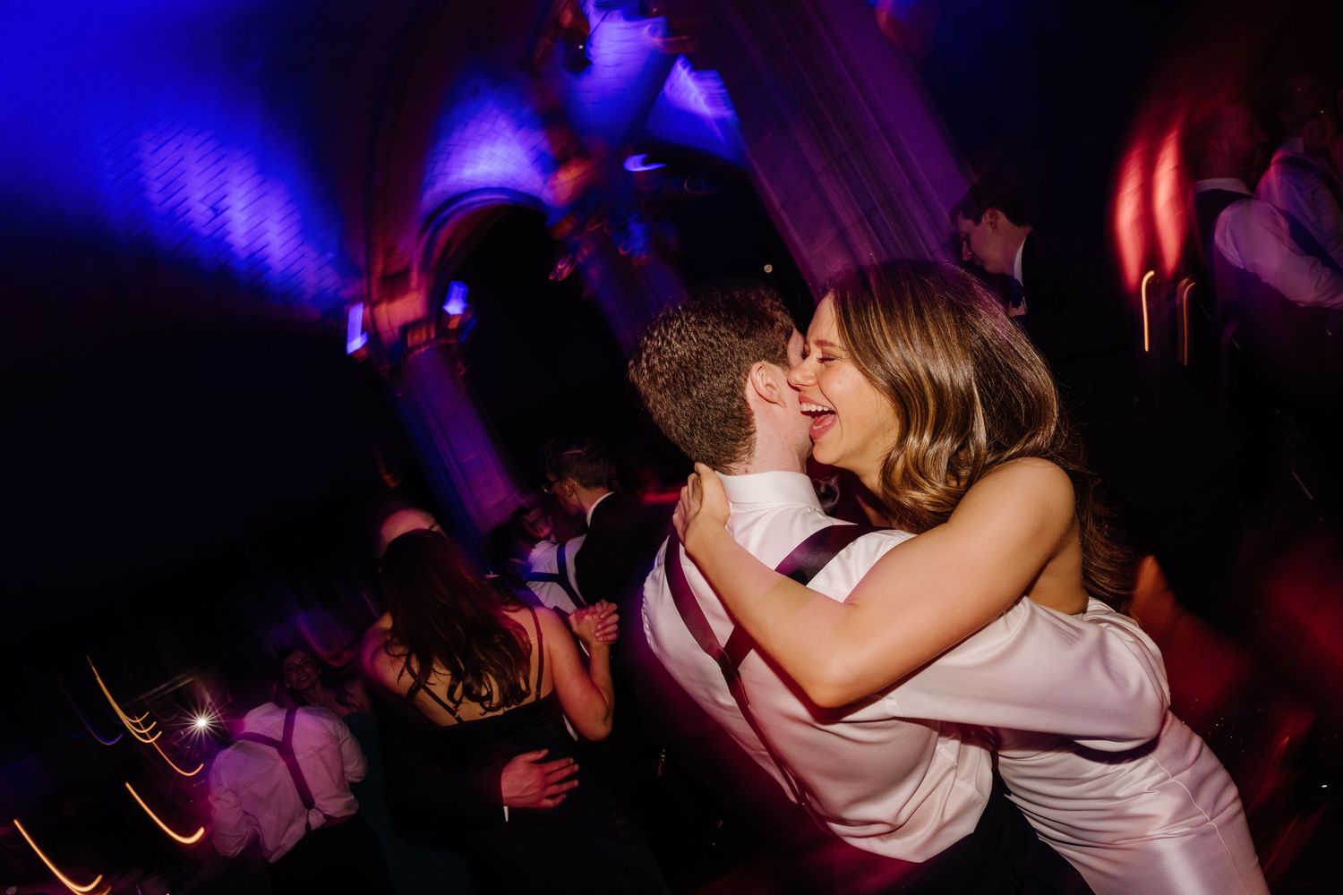 Bride and groom sharing romantic kiss on colorful dance floor at wedding reception.
