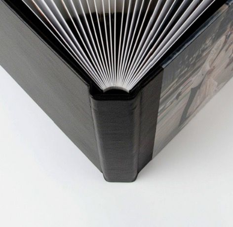Close-up of a black hardcover photo album spine showing fanned pages and elegant textured cover with printed photos.