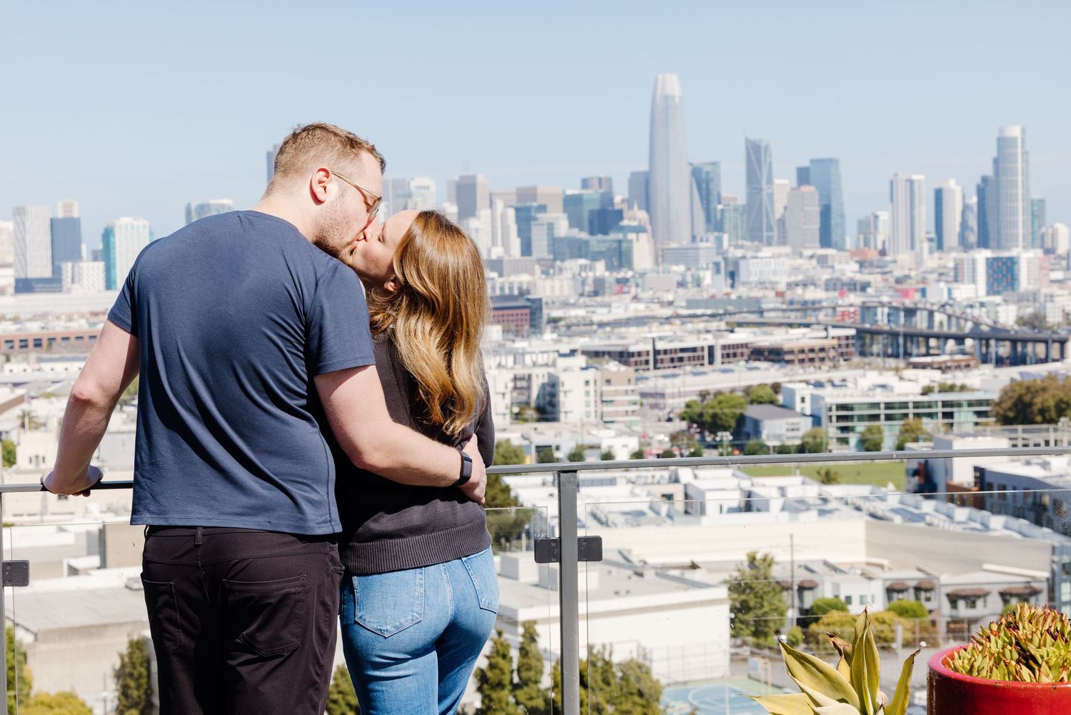 Couple sharing a romantic kiss with the San Francisco skyline as a stunning backdrop on a clear day.