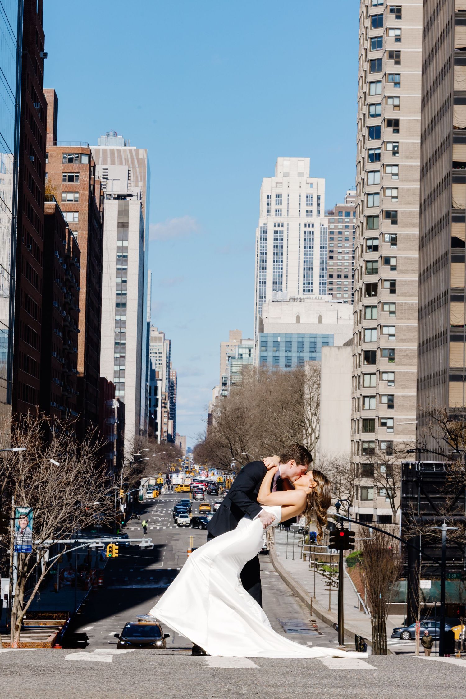 Groom dips bride for a kiss on a New York City street with skyline in background.