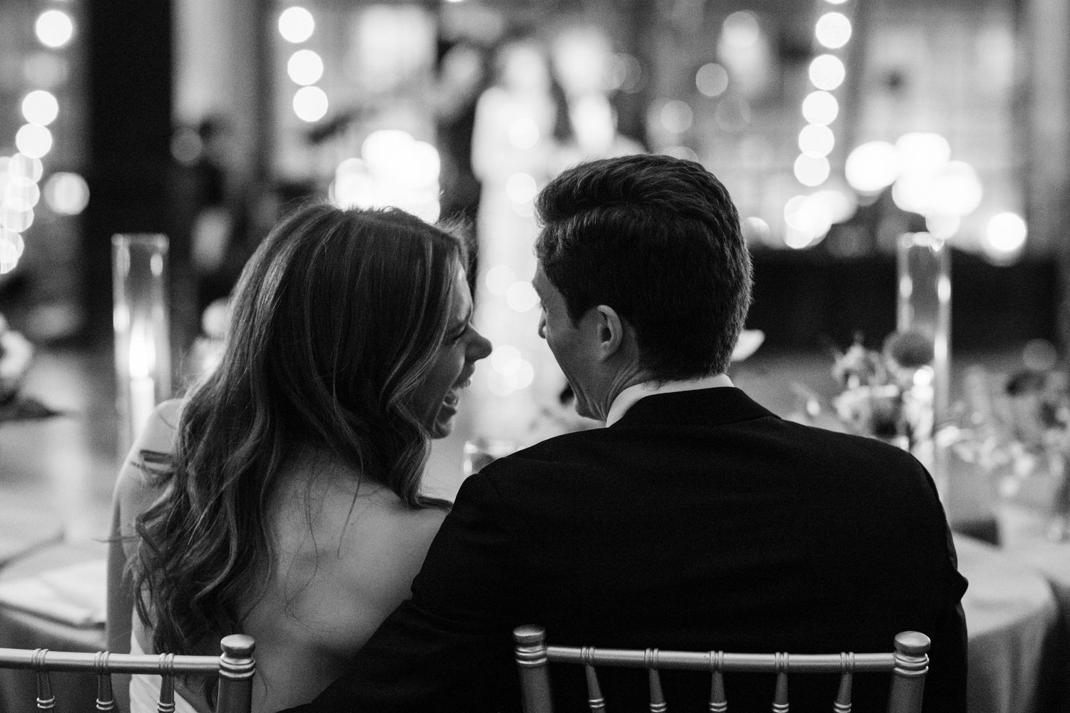 Black and white photo of bride and groom sharing intimate moment at wedding reception table.
