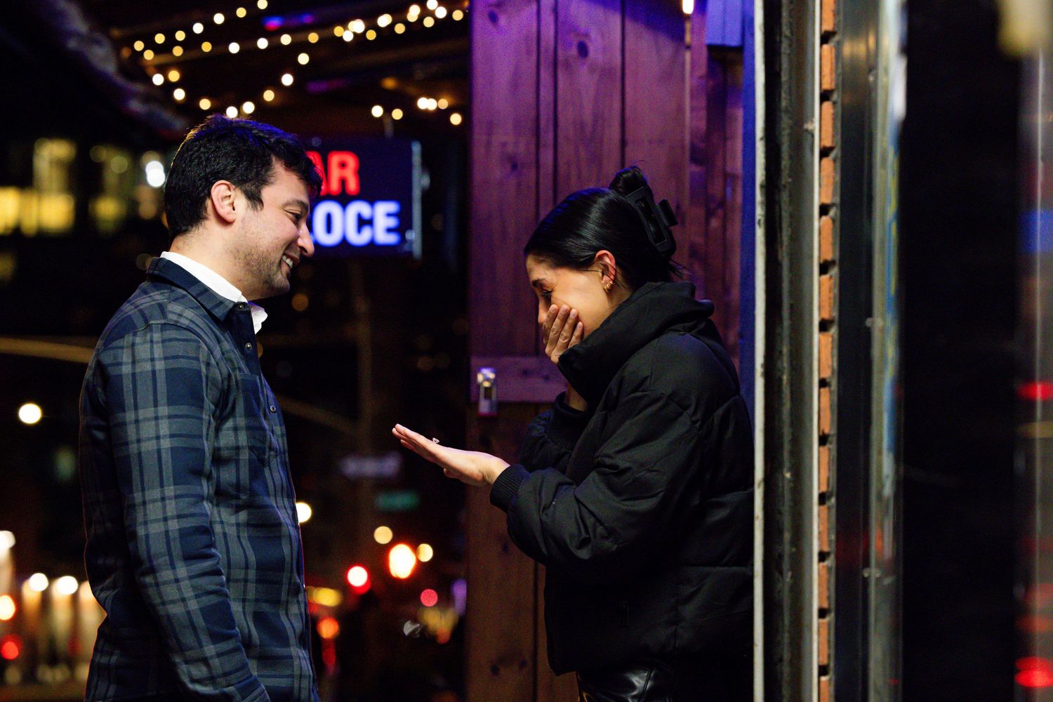 Man and woman share a romantic moment outside Bar Veloce restaurant at night with bokeh city lights behind them.