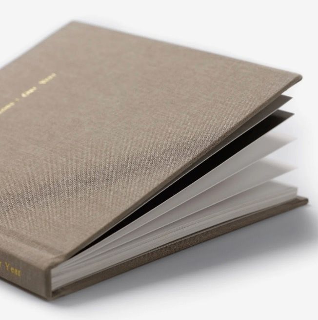Close-up of an open hardcover linen journal with gold foil text and thick white pages.