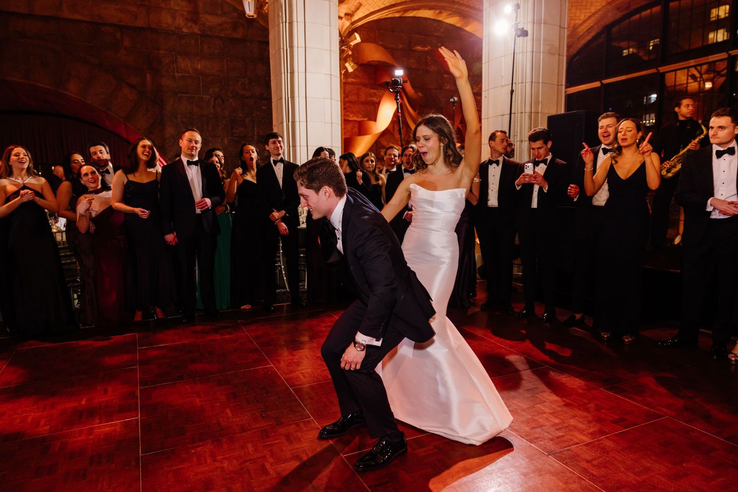Groom dips bride on the dance floor as elegantly dressed wedding guests cheer and applaud.