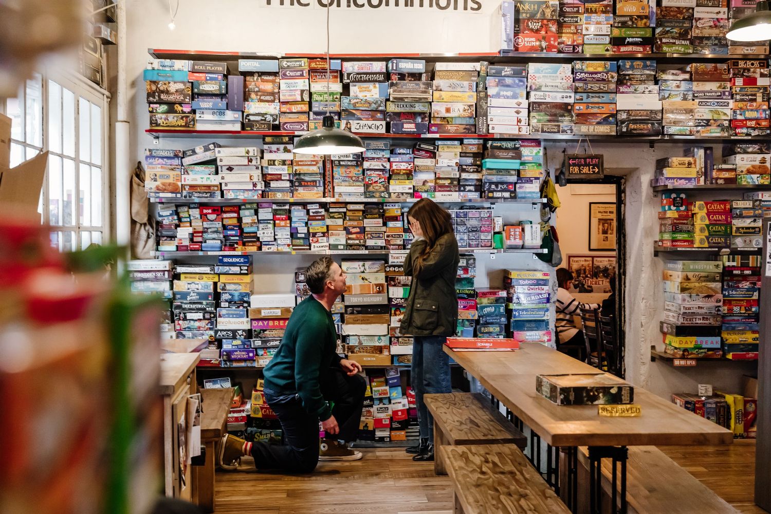 Man proposing on one knee in The Uncommons board game cafe surrounded by shelves of games.