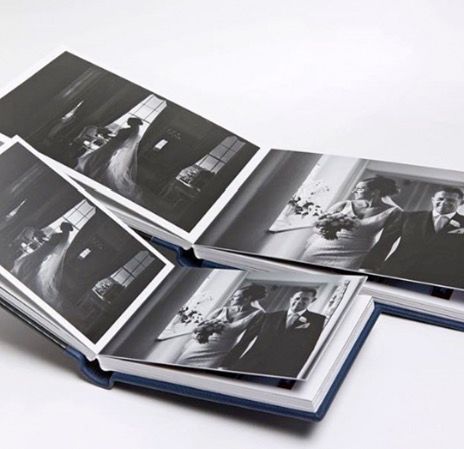 Three open photo albums displaying black and white wedding photography prints, stacked on a white surface.