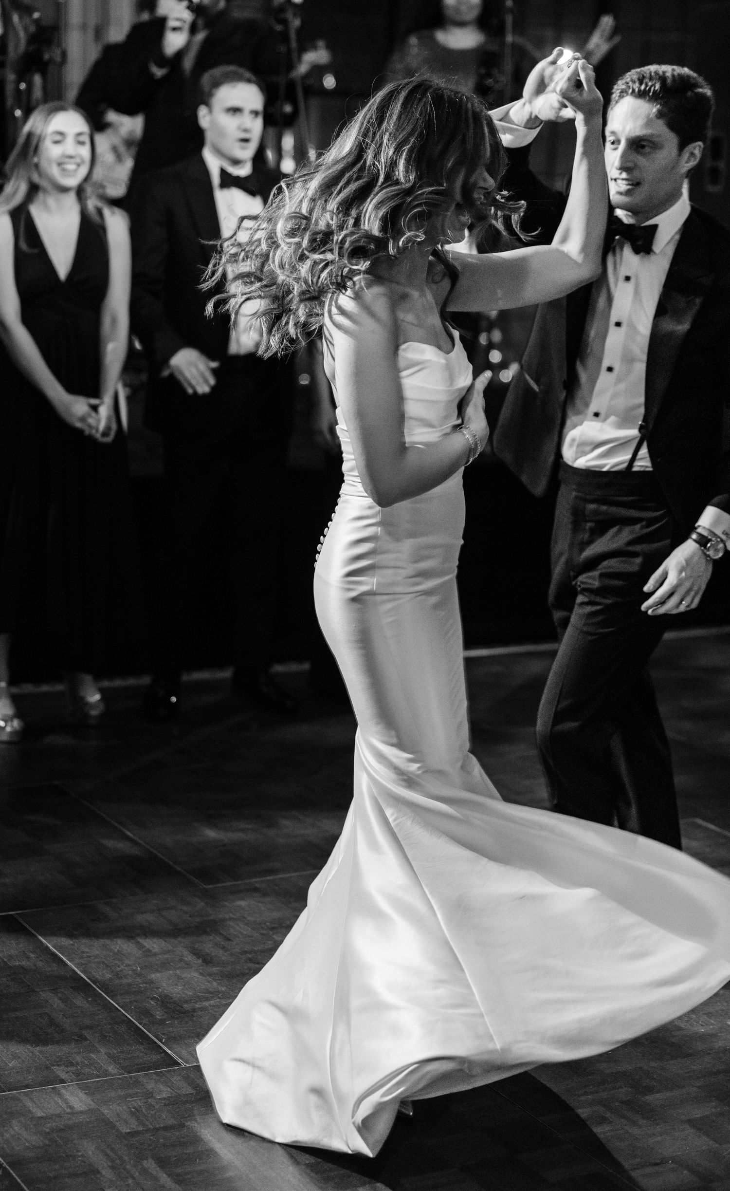 Bride twirls in her elegant mermaid gown during first dance as guests watch in black and white.