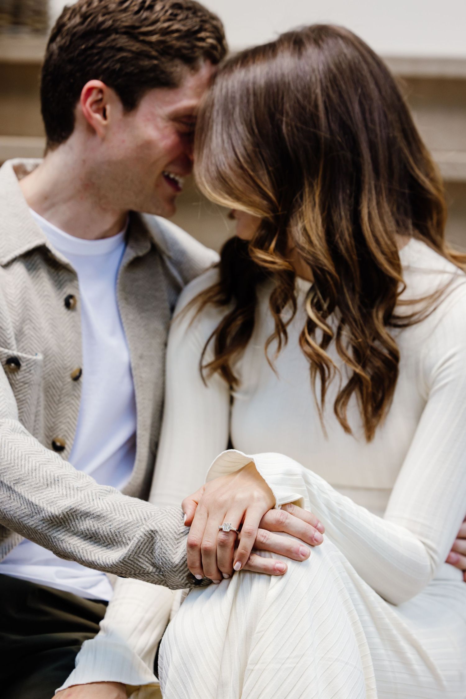 Couple sharing an intimate moment, woman displaying her engagement ring while leaning close together.