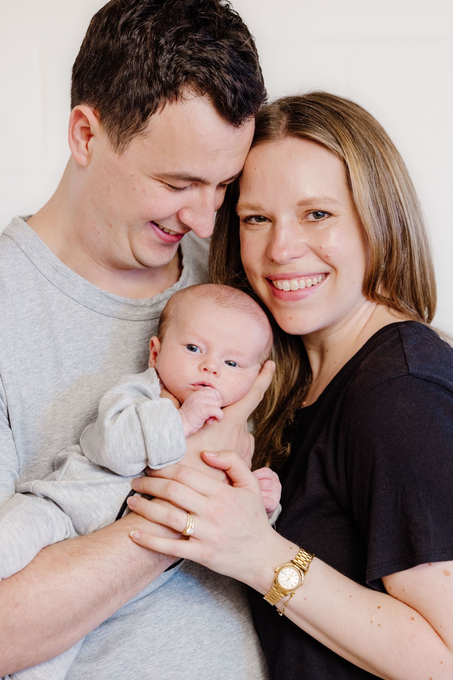 Happy couple smiling and holding their newborn baby together against a white background.