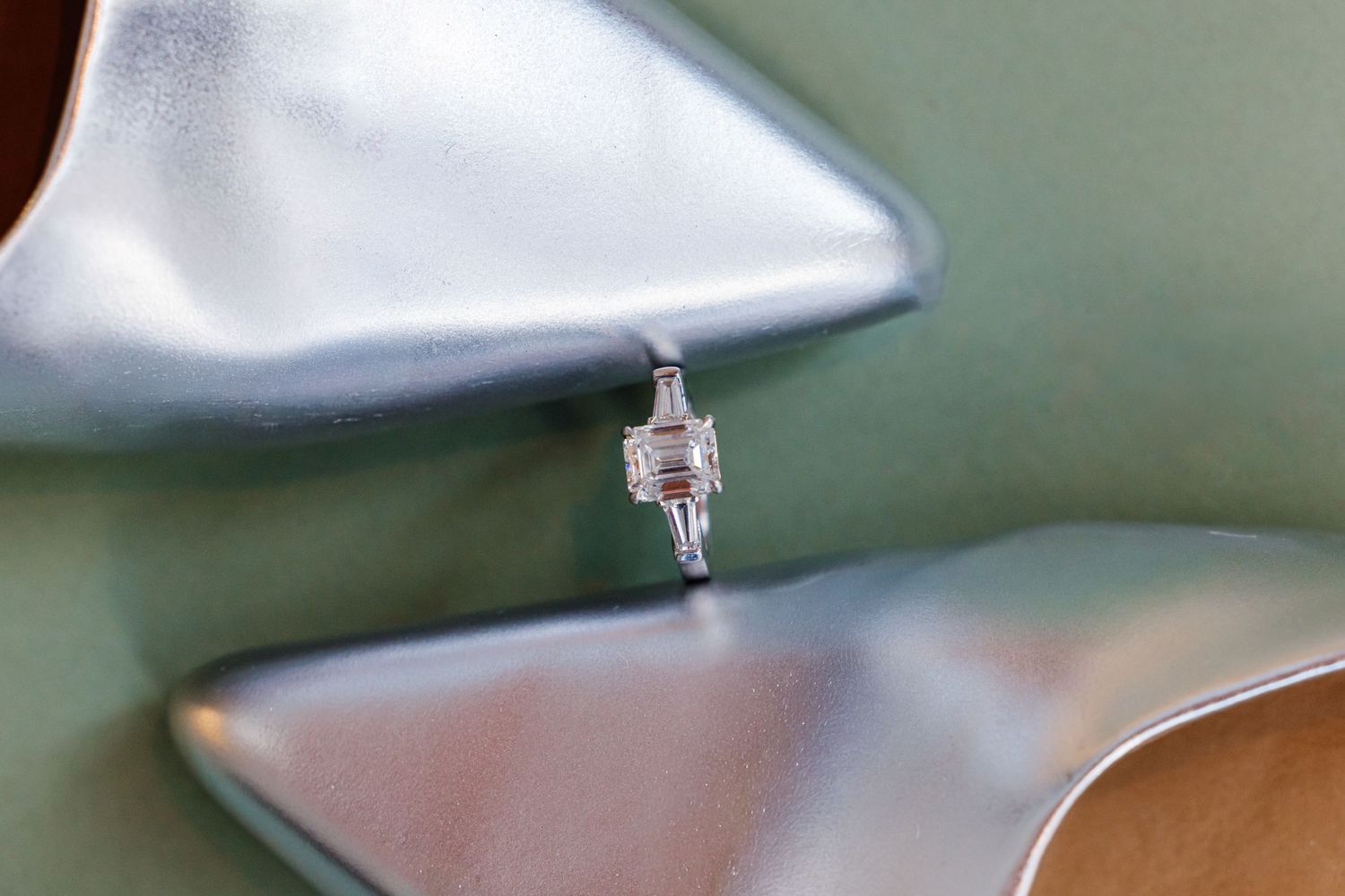 Emerald cut diamond engagement ring balanced between silver pointed-toe stiletto heels.