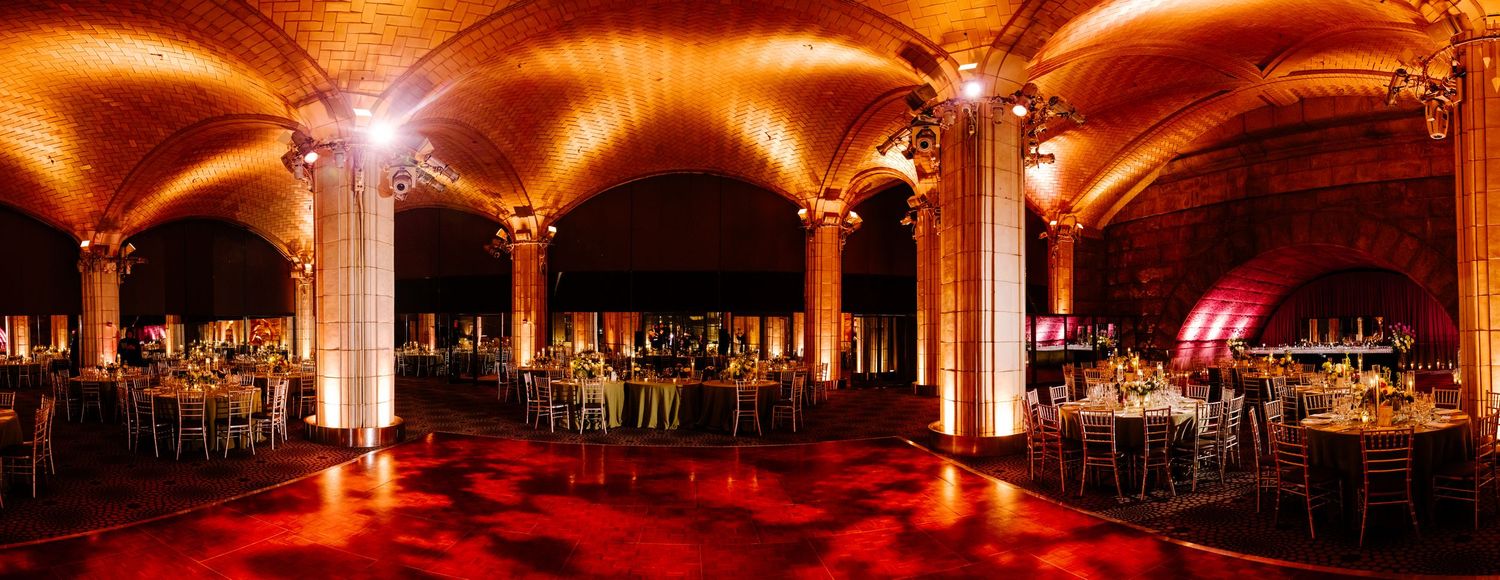Grand wedding reception hall with dramatic amber uplighting illuminating arched brick ceilings and columns.