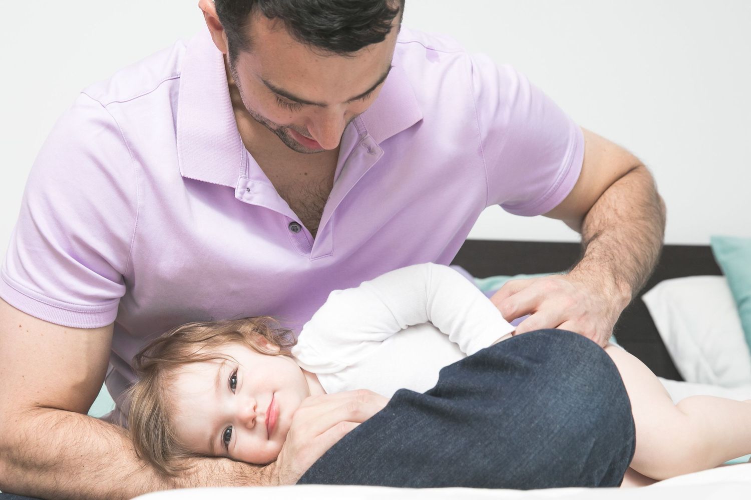 Father smiling at his baby lying on a bed, sharing a tender bonding moment together.
