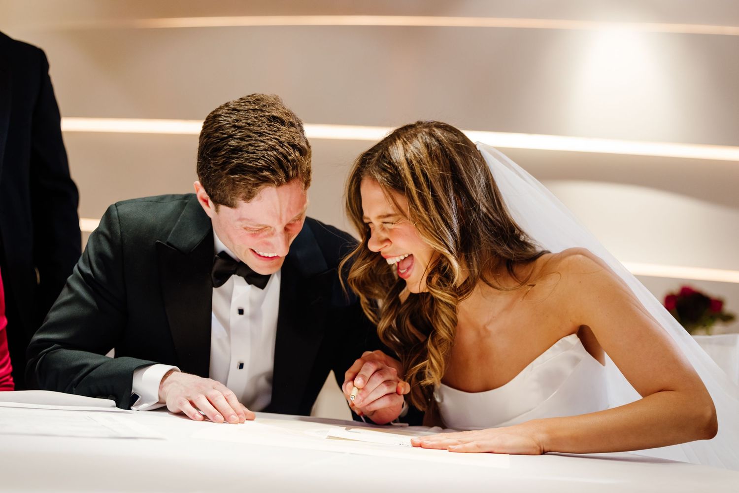 Newlyweds sharing joyful intimate moment while signing marriage certificate at wedding ceremony.