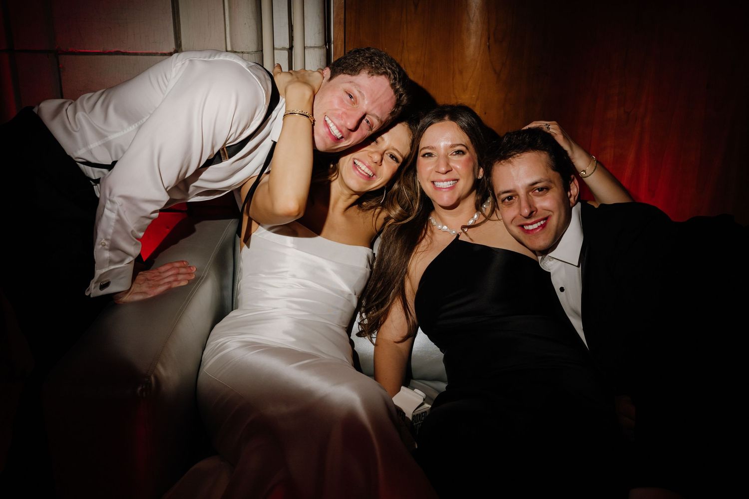 Bride, groom, and two friends posing together happily on a couch at a wedding reception.