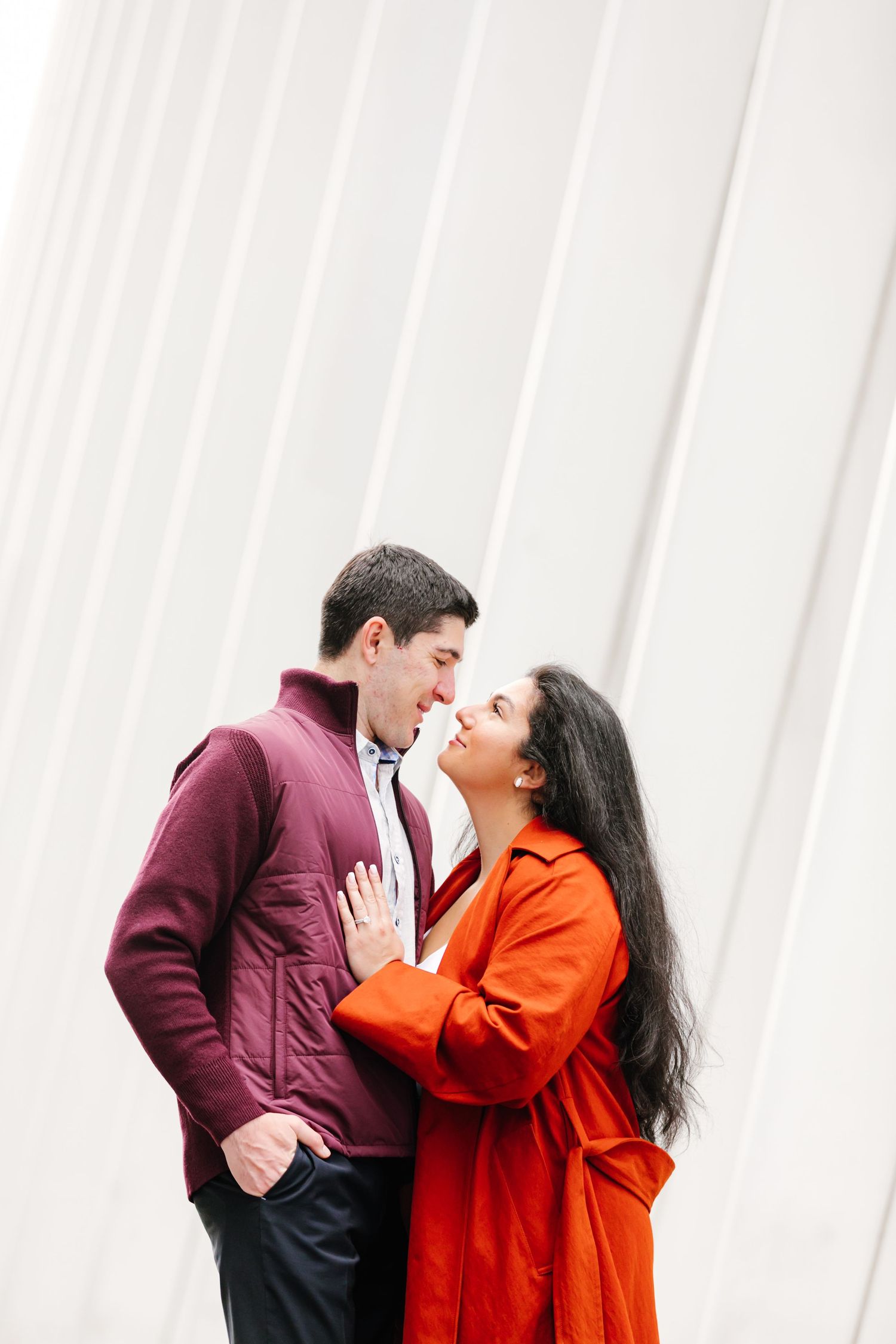 Couple in colorful coats leaning in for a kiss against a modern white architectural background.