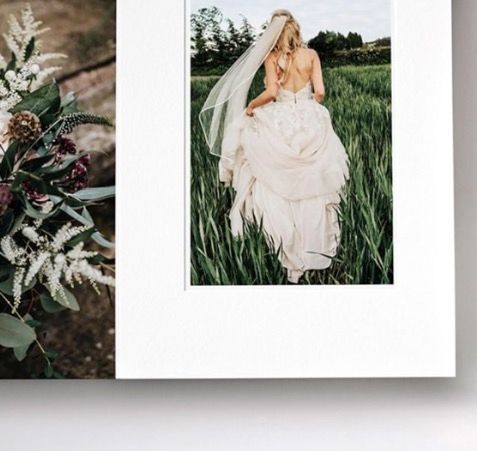 A bride in a flowing white wedding dress and veil stands in a lush green field, with a floral bouquet arrangement nearby.