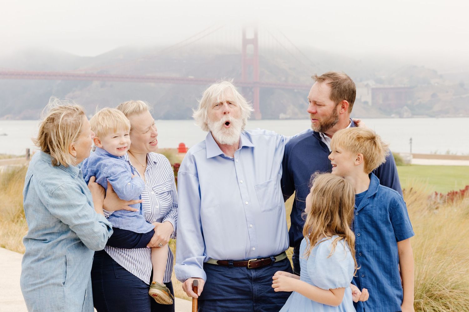 Multi-generational family laughing together near Golden Gate Bridge on a foggy day.