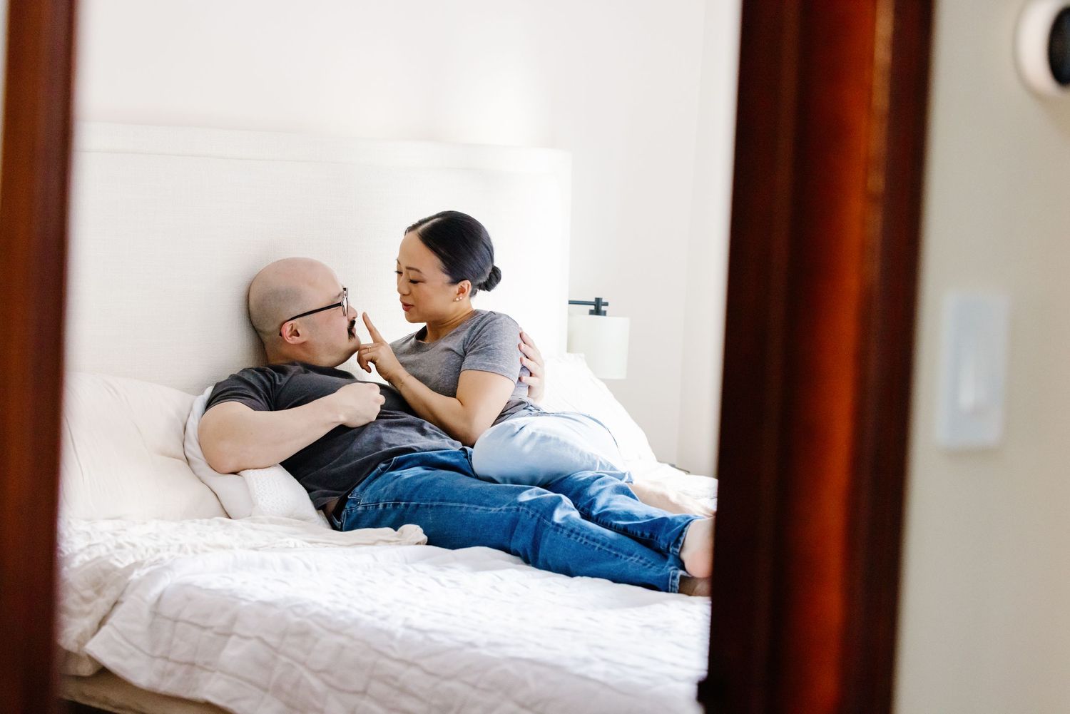 Couple relaxing together on white bed in cozy bedroom during intimate lifestyle photo session.