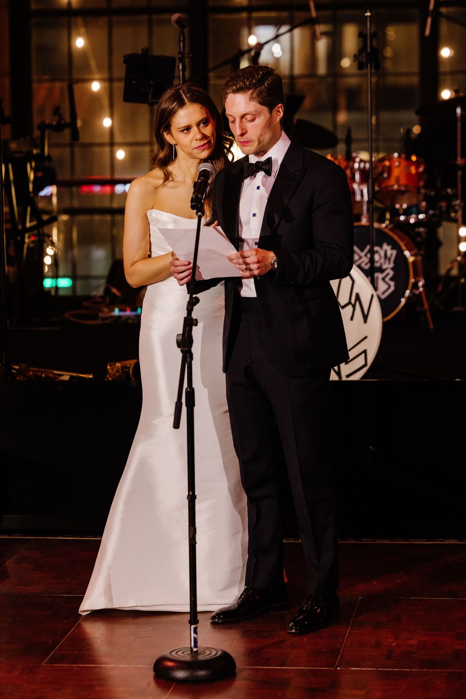 Bride and groom reading vows together at microphone stand during elegant wedding reception.