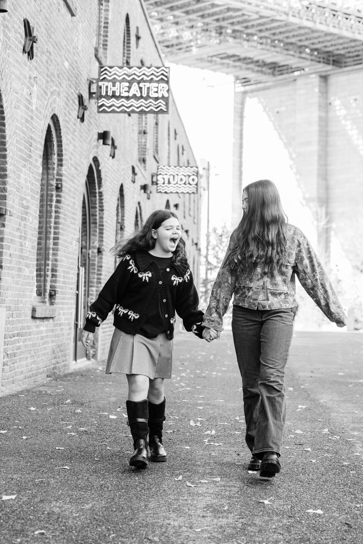 Black and white photo of two laughing girls holding hands outside a theater in Brooklyn.