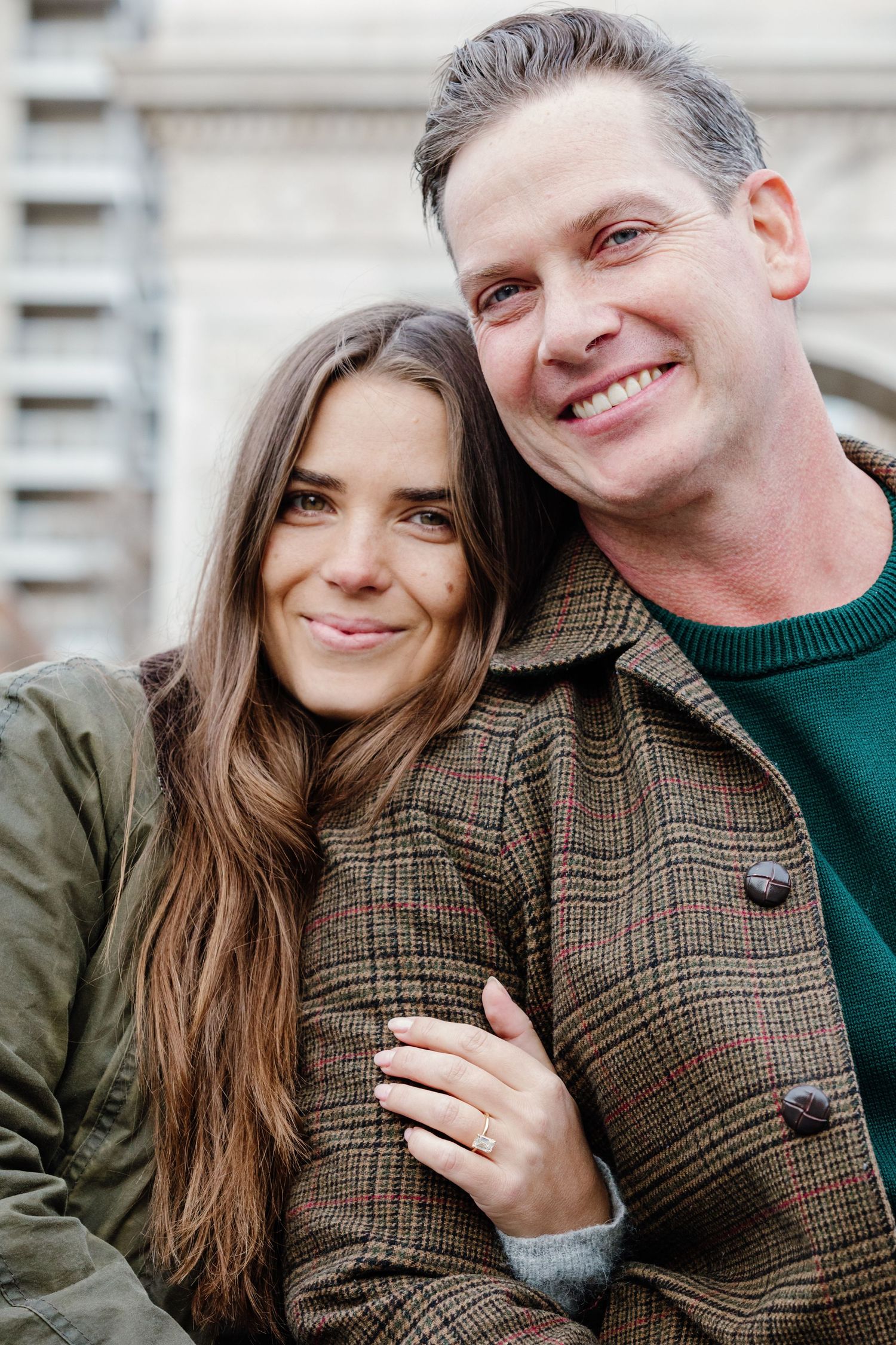 Happy newly engaged couple smiling outdoors, woman showing engagement ring on her finger.