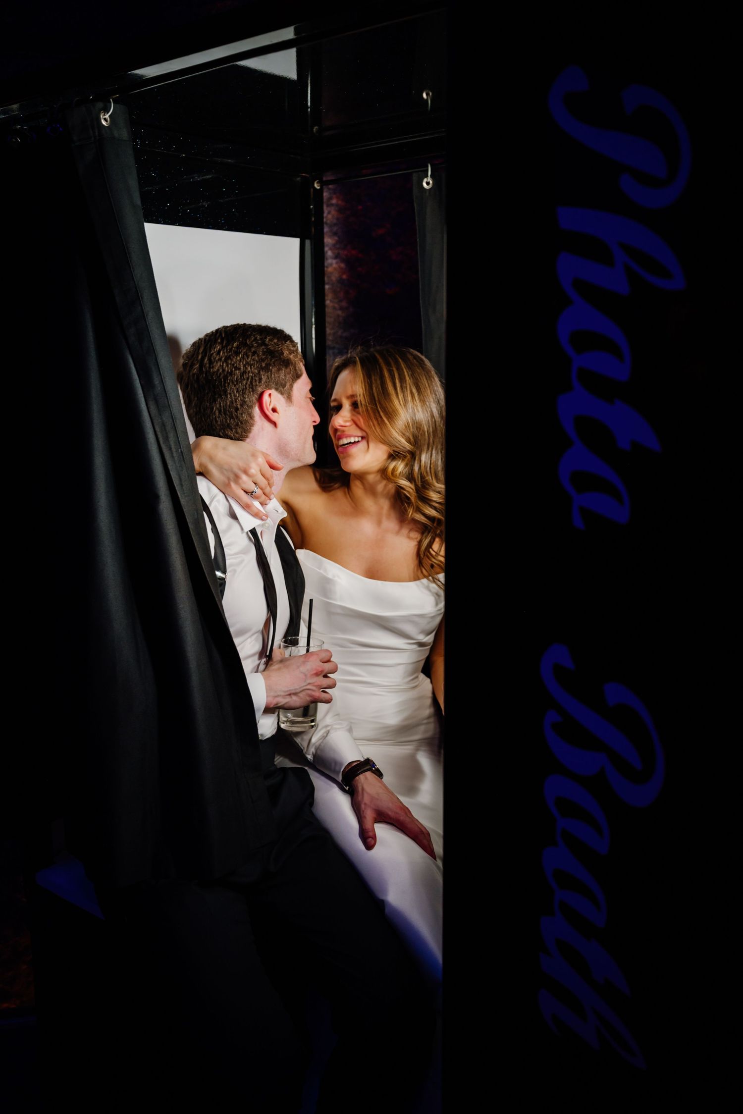 Bride and groom sharing intimate moment inside photo booth at wedding reception.