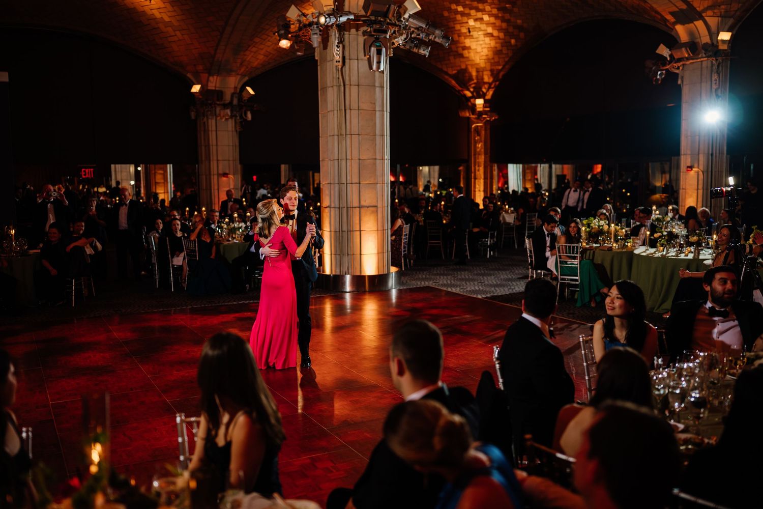 Guest in pink gown performing speech on dance floor of grand wedding reception venue.