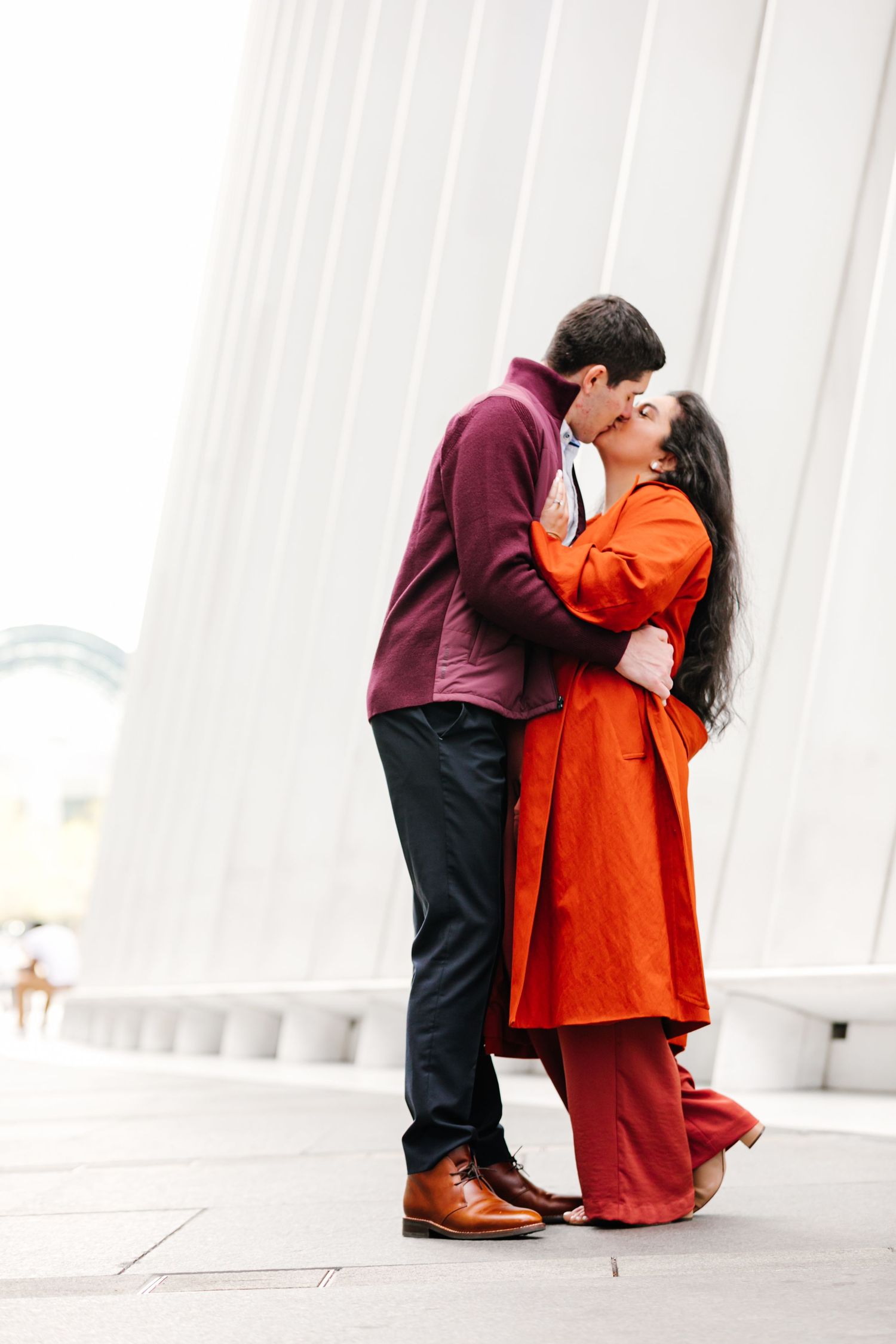 Couple sharing a romantic kiss in front of a striking white architectural structure during engagement shoot.