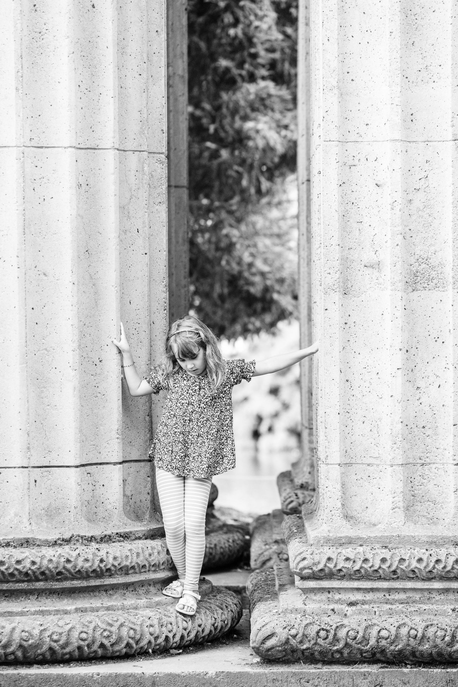 Black and white photo of young girl posing between stone columns at Palace of Fine Arts.