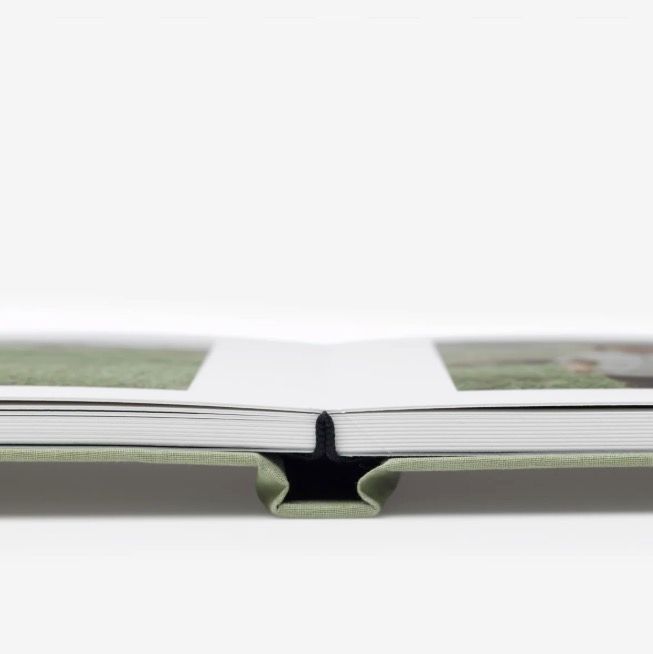 Close-up side view of an open photo book with green cover and layflat binding on white background.