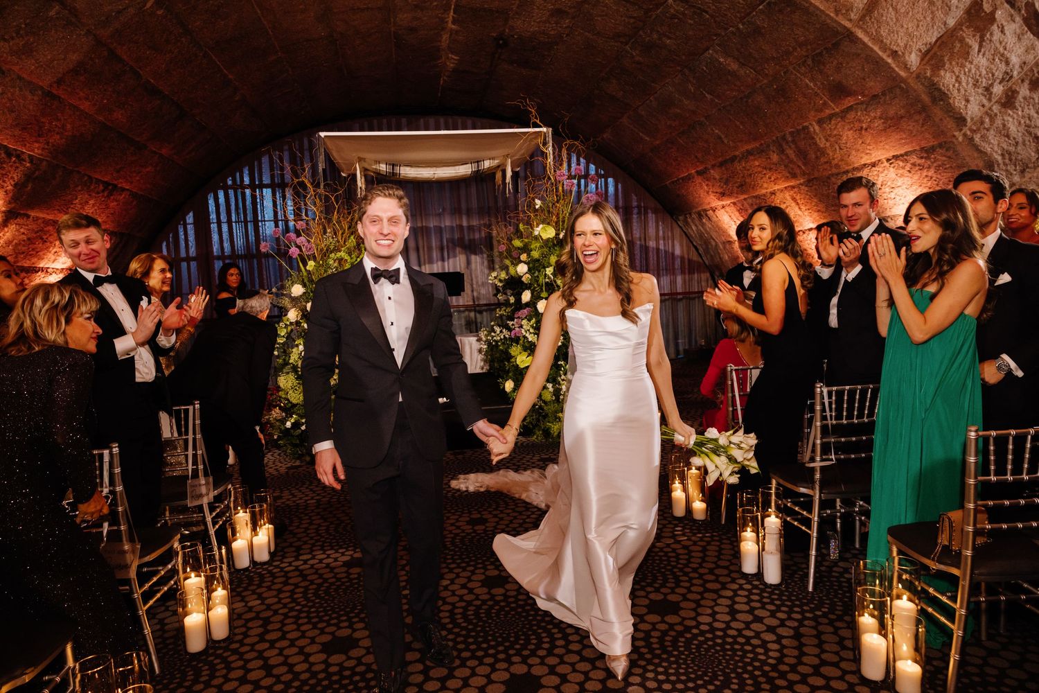 Newlyweds joyfully walk back down the aisle hand-in-hand after their candlelit wedding ceremony.