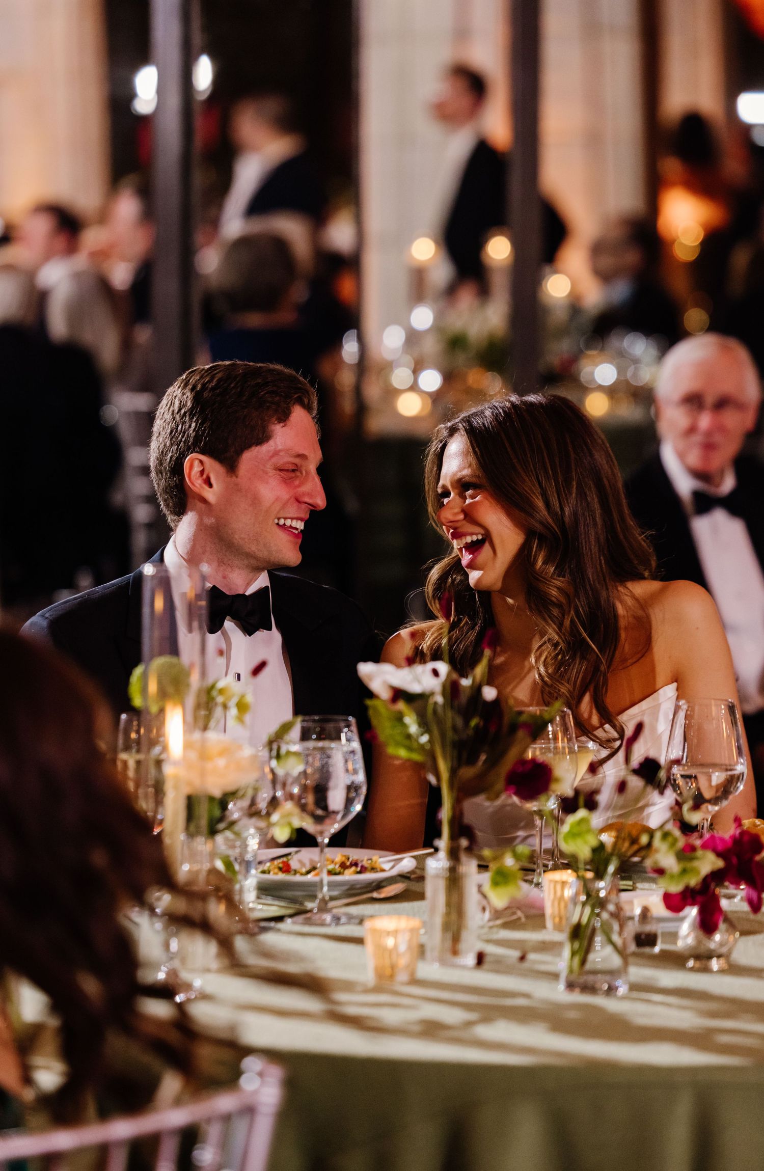 Bride and groom laughing joyfully together at candlelit wedding reception dinner table.