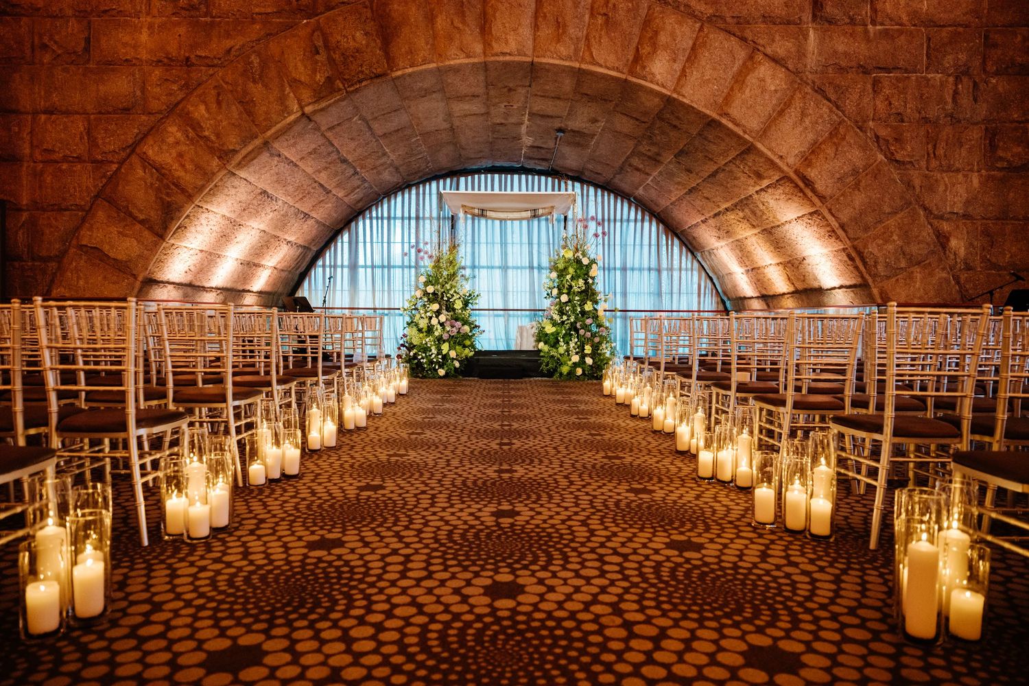 Elegant wedding ceremony venue with arched ceiling, candlelit aisle, and Christmas tree backdrop.