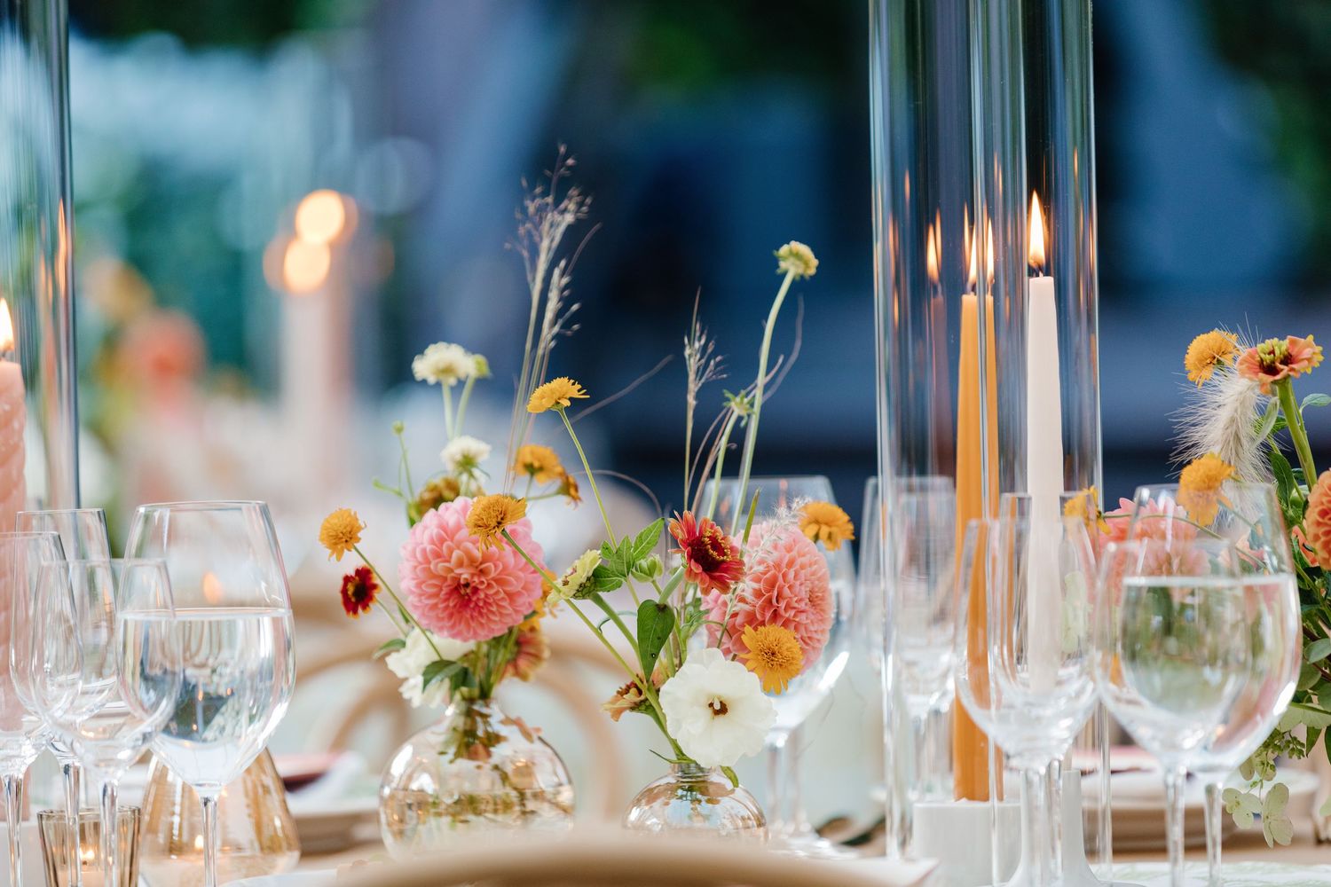 Colorful floral wedding table centerpiece with pink dahlias, candles, and crystal glassware.
