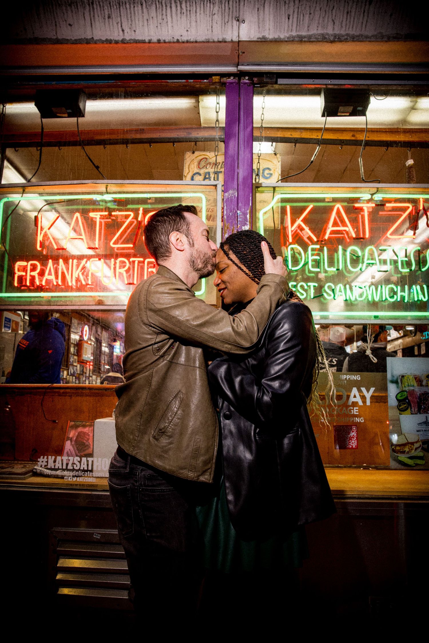Couple sharing a romantic moment kissing in front of glowing neon signs at Katz's Delicatessen in NYC.