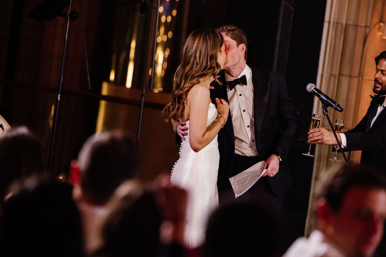 Newlyweds share romantic kiss on stage during wedding reception before guests.