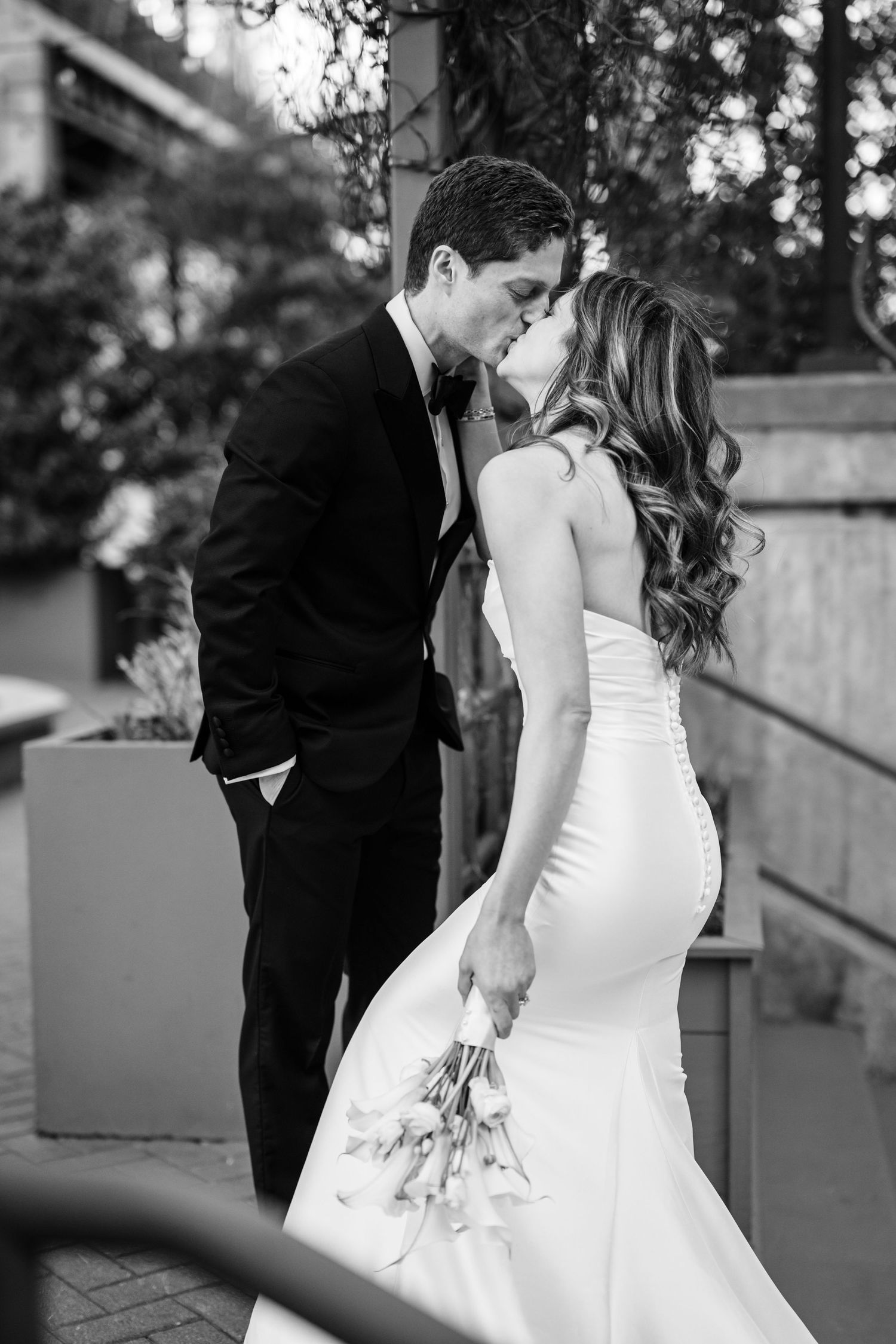 Black and white photo of a bride and groom sharing a romantic kiss while she holds a bouquet.