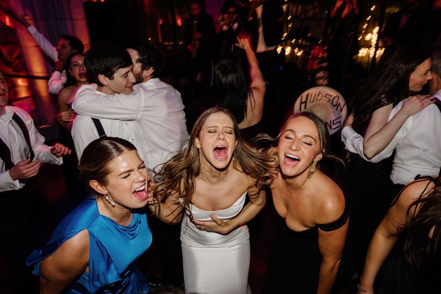 Bride and three friends laughing and dancing together joyfully on a wedding reception dance floor.