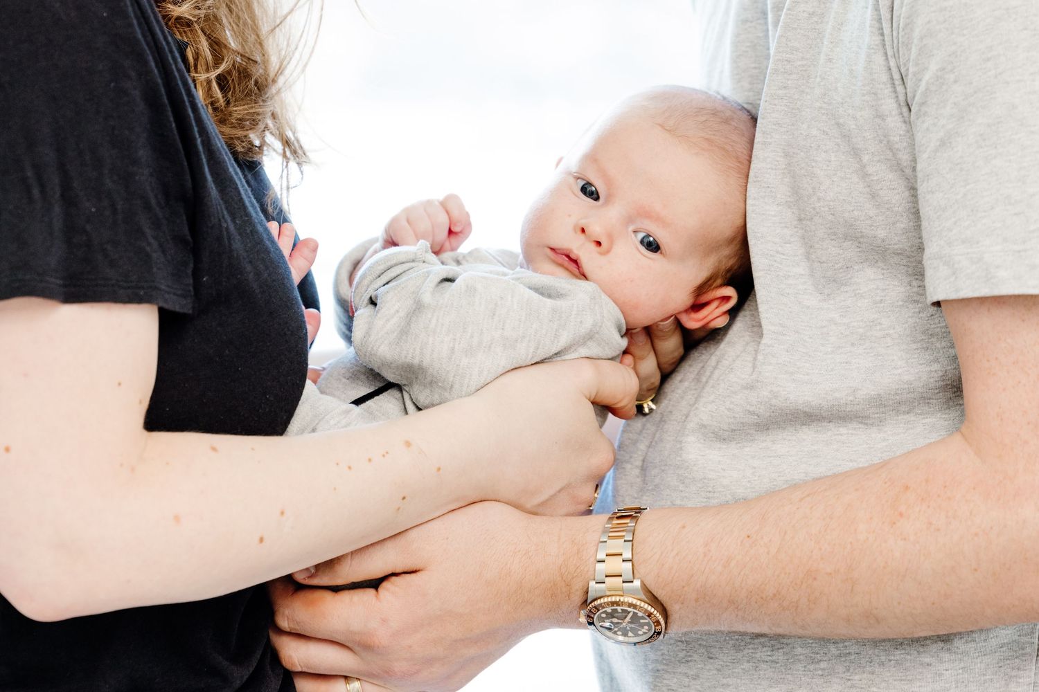 Two parents lovingly cradling their newborn baby, with father wearing a gold watch.
