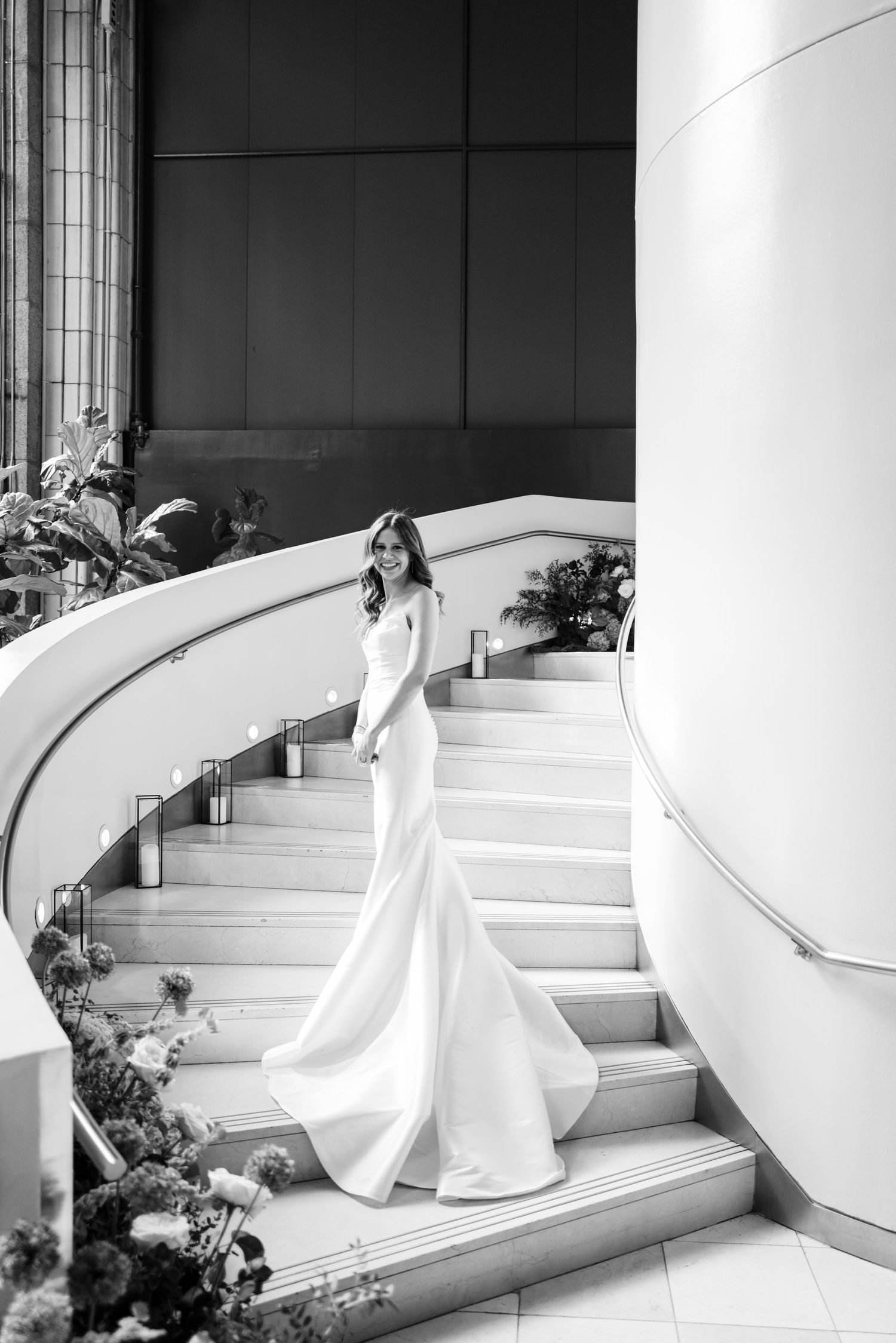 Black and white portrait of bride in elegant mermaid gown posing on curved marble staircase.