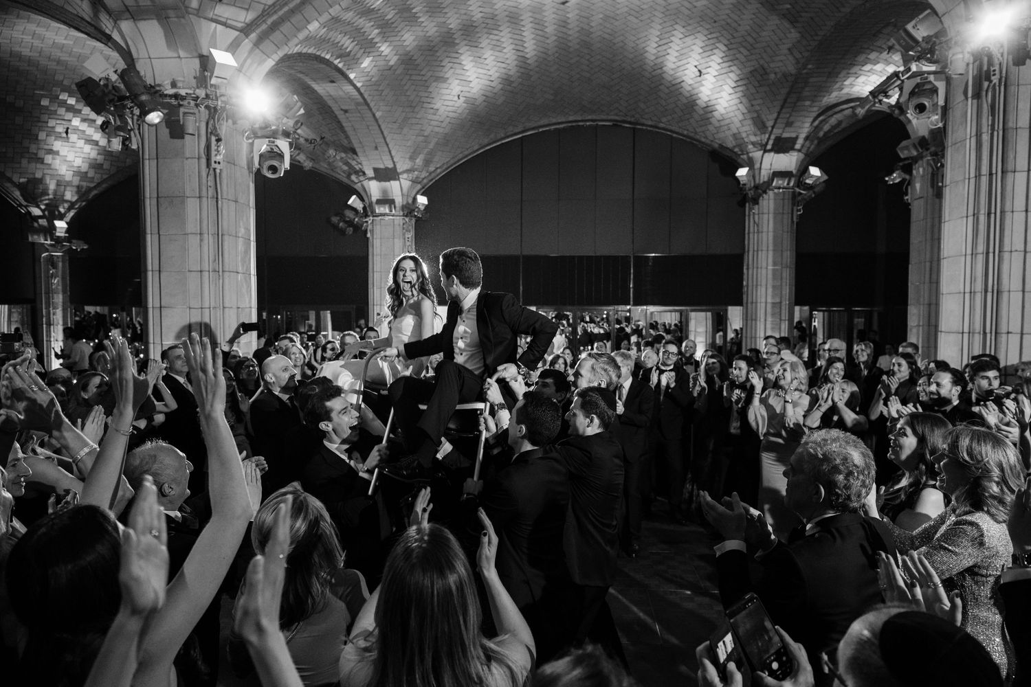 Bride and groom are lifted by cheering guests in a stunning black and white wedding celebration photo.