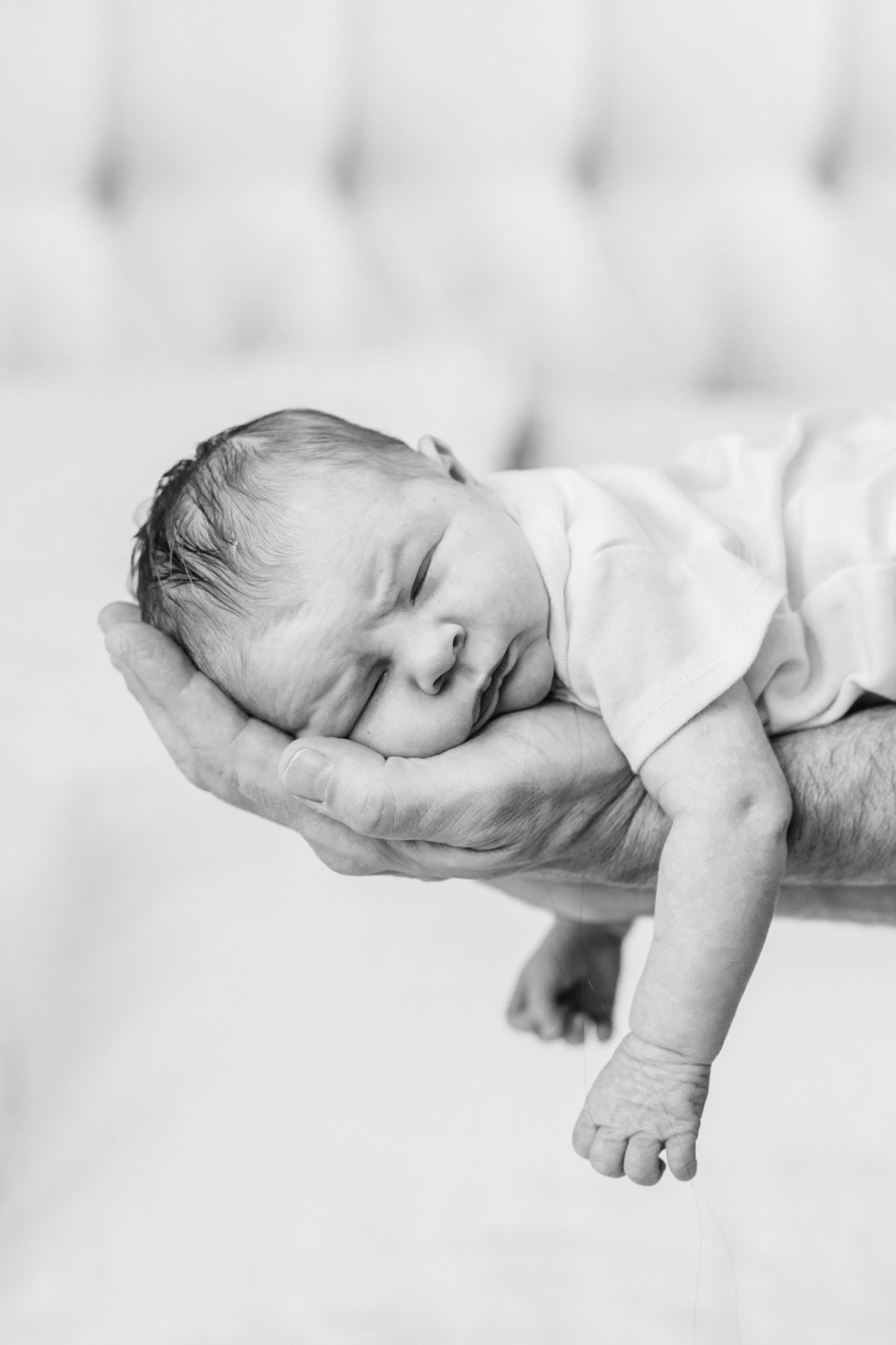 Black and white photo of a sleeping newborn baby cradled gently in an adult's hand against soft background.