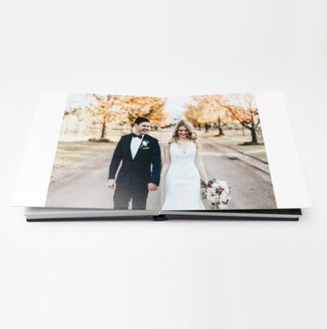 Open wedding photo book displaying a bride and groom walking together outdoors among autumn trees.