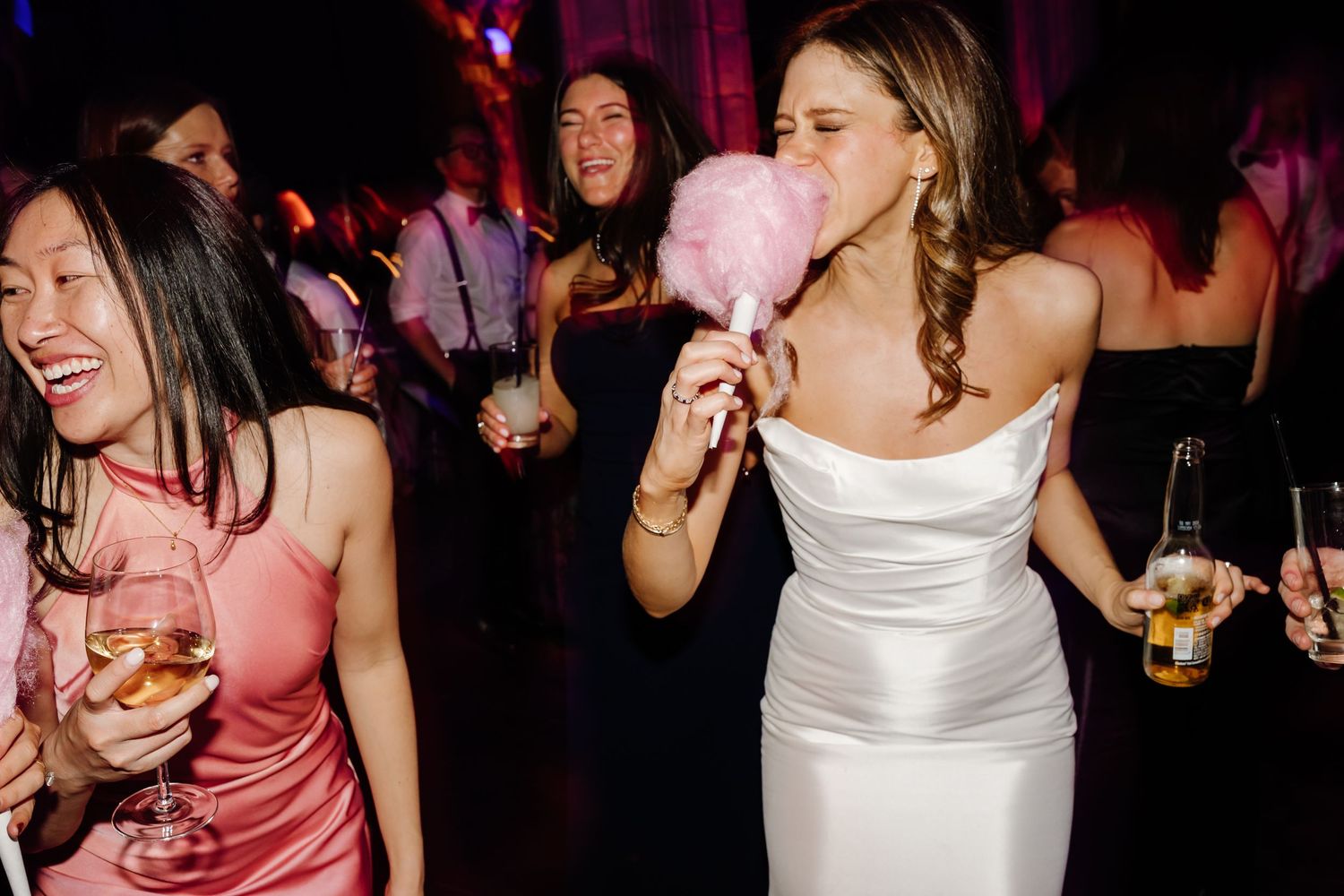Bride eating pink cotton candy while dancing with guests at lively wedding reception.