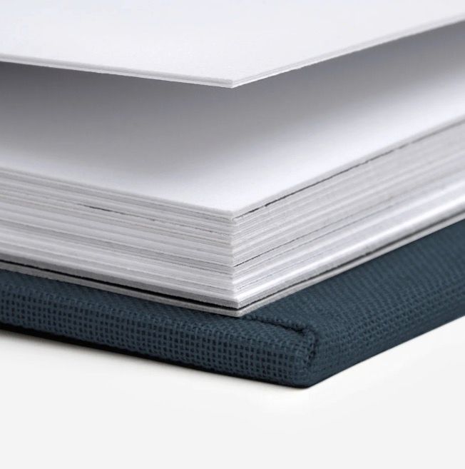 Stack of white paper sheets resting on a dark navy blue textured hardcover book binding.